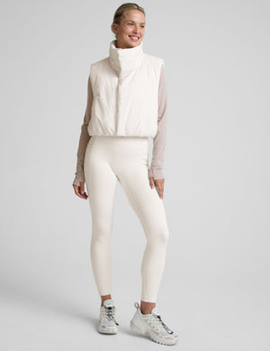 model wearing a white puffer vest over a long-sleeve shirt on a light gray background. 