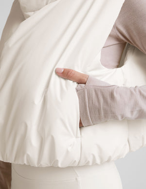 model wearing a white puffer vest over a long-sleeve shirt on a light gray background. 