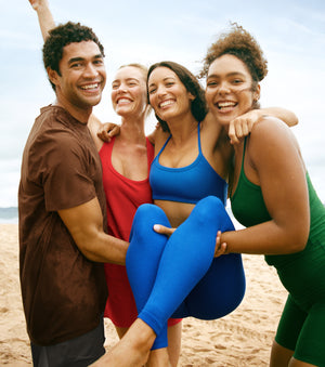 model on left is wearing a brown men's t-shirt. model on center left is wearing a red mini halter dress. model on center right is wearing a blue bra top and blue high-waisted midi leggings. model on right is wearing a green tank top and green high-waisted biker shorts. 