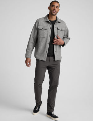model wearing a gray men's button up jacket over a black shirt on a light gray background. 