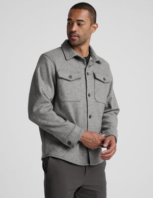 model wearing a gray men's button up jacket over a black shirt on a light gray background. 