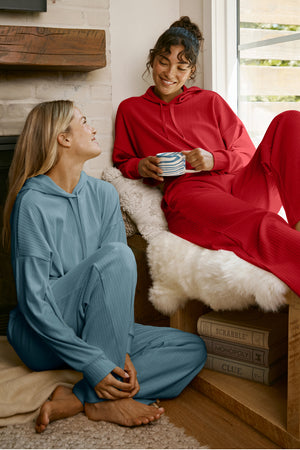 Two women sitting together wearing red and blue ribbed lounge sets. 