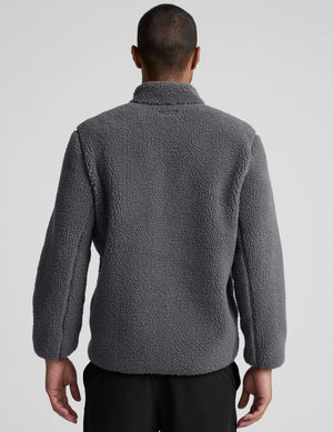 man wearing a gray fleece zip-up jacket against a plain background. 