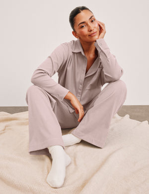 Woman wearing a corduroy pants with a matching button down shirt on a light background. 