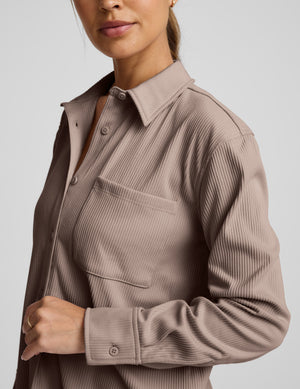 Woman wearing a brown corduroy button-up shirt and pants on a light gray background. 
