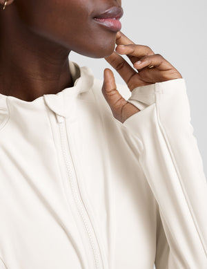 woman wearing a white athletic hooded jacket and leggings on a plain background. 