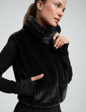 woman wearing a black faux fur vest against a plain background. 