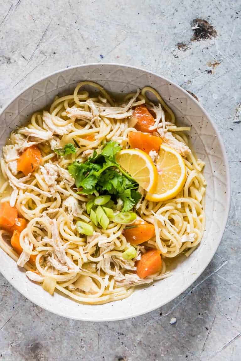 overhead view of instant pot chicken soup in a white bowl with garnish on top