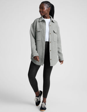 woman wearing a gray shirt jacket against a plain background. 