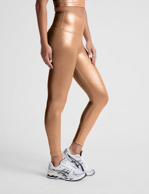 woman wearing copper metallic midi leggings against a light gray background. 