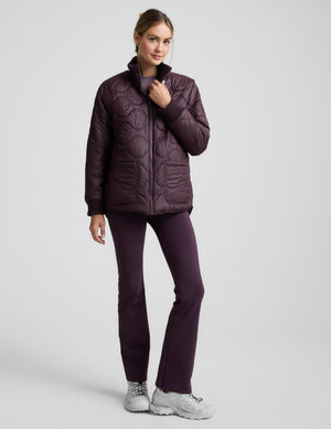 Woman wearing a quilted and boucle purple jacket on a light gray background. 