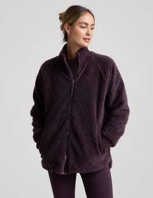 Woman wearing a quilted and boucle purple jacket on a light gray background. 