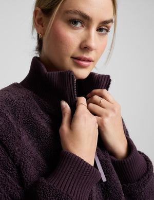 Woman wearing a quilted and boucle purple jacket on a light gray background. 