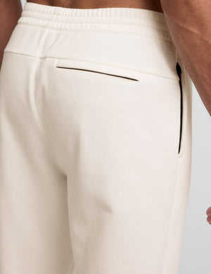 man wearing a gray crew neck t-shirt and white fleece sweatpants on a plain background. 