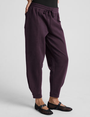 model is wearing purple fleece barrel style fleece sweatpants against a plain background. 