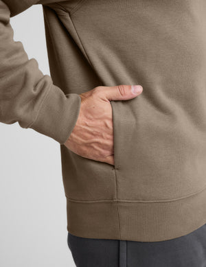 Man wearing a brown half-zip sweatshirt against a light gray background. 