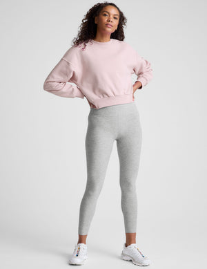 woman wearing a light pink sweatshirt and gray leggings on a plain background. 