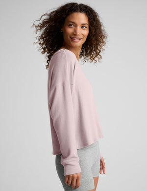 woman wearing a light pink off-shoulder sweater against a plain background. 