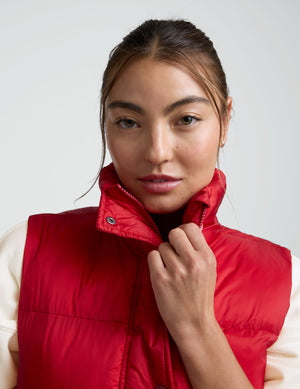 woman wearing a red puffer vest and leggings against a plain background. 
