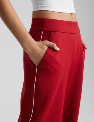 Red wide-leg pants with white piping on a light gray background. 