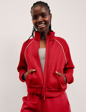 woman wearing a red zip-up jacket with white piping against a plain background. 