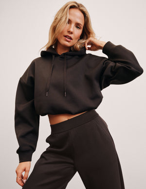 woman wearing a brown cropped hoodie and pants against a plain background. 
