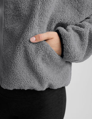 model wearing a gray fleece zip-up jacket against a plain background. 