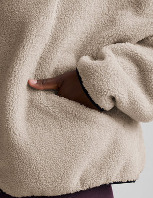 model wearing a beige zip-up fleece jacket against a plain background. 