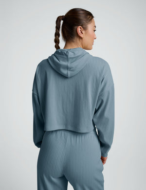 woman wearing a blue ribbed cropped hoodie and pants on a plain background. 