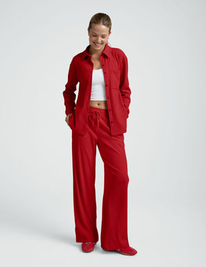 woman wearing a red ribbed button down shirt and red ribbed lounge pants against a plain background. 