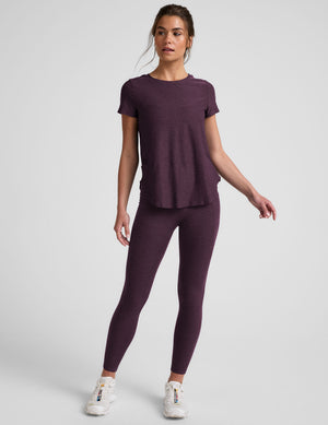 model wearing a purple t-shirt and purple high-waisted midi length leggings with pockets on a light gray background. 