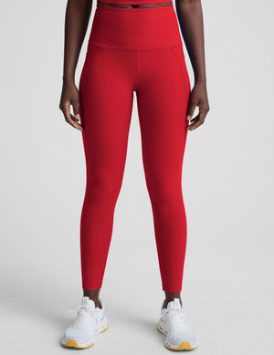 woman wearing a red high-waisted midi length pocket leggings on a plain background. 