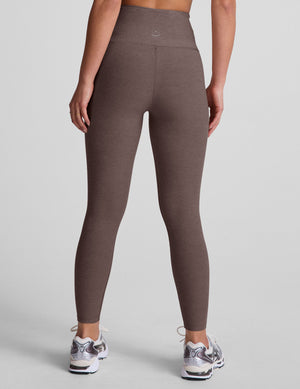 Brown leggings with a crossover front waistband worn by a person on a plain background. 