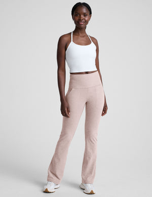woman wearing a white racerback cropped tank and pink pants against a plain background. 