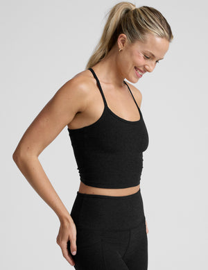 woman wearing a black racerback cropped tank and leggings on a plain background. 