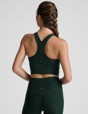 woman wearing a green high-neck racerback cropped tank and leggings on a plain background. 