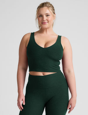 woman wearing a green soft v-neck cropped tank and joggers against a plaind background. 
