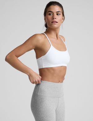 woman wearing a white slim racerback sports bra and gray leggings on a plain background. 