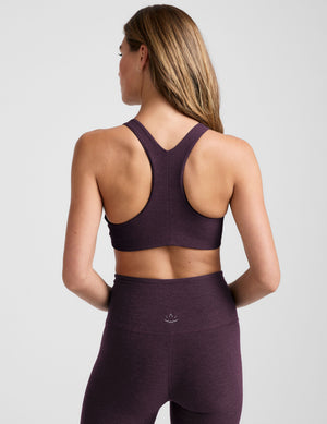 model wearing a purple high-neck racerback bra and leggings on a light gray background. 