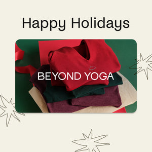Stack of red, green, and maroon yoga pants with 'Beyond Yoga' branding and 'Happy Holidays' text on a decorative card.
