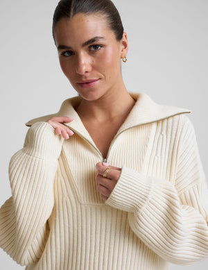 woman wearing a white quarter zip collared sweater against a plain background. 